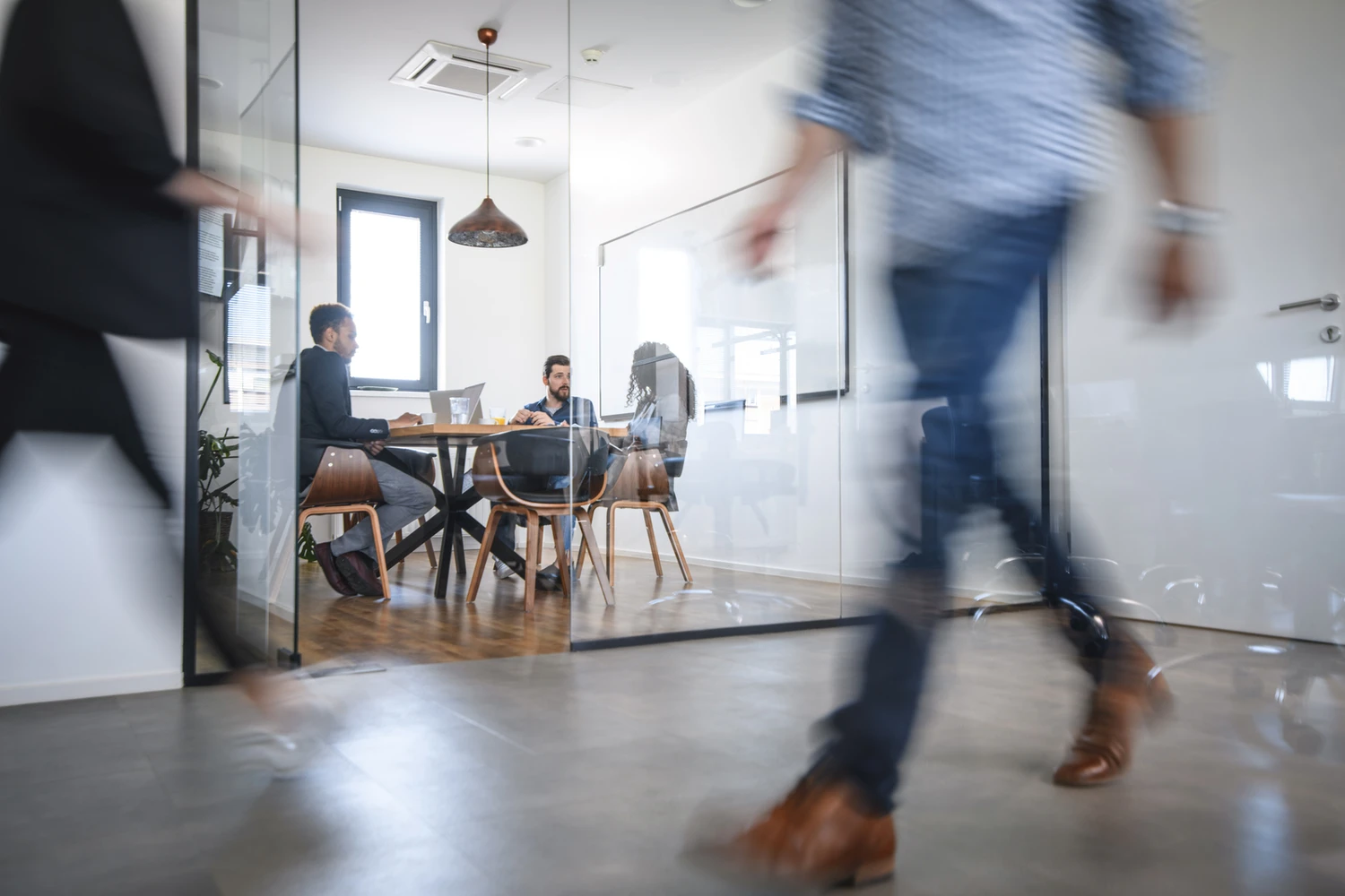 © iStock Man walking in an office with people attending a meeting